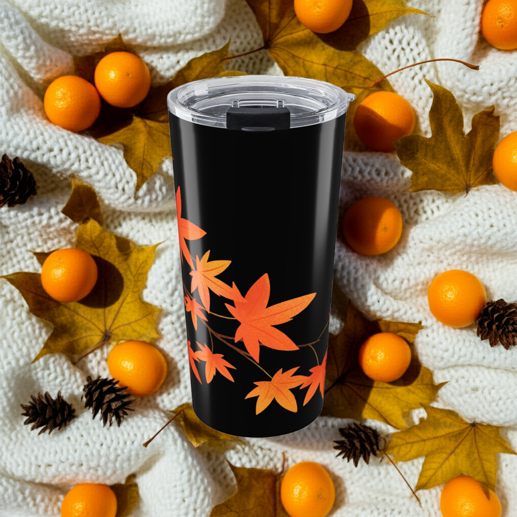 Black tumbler with orange leaf pattern surrounded by oranges and leaves on a textured surface
