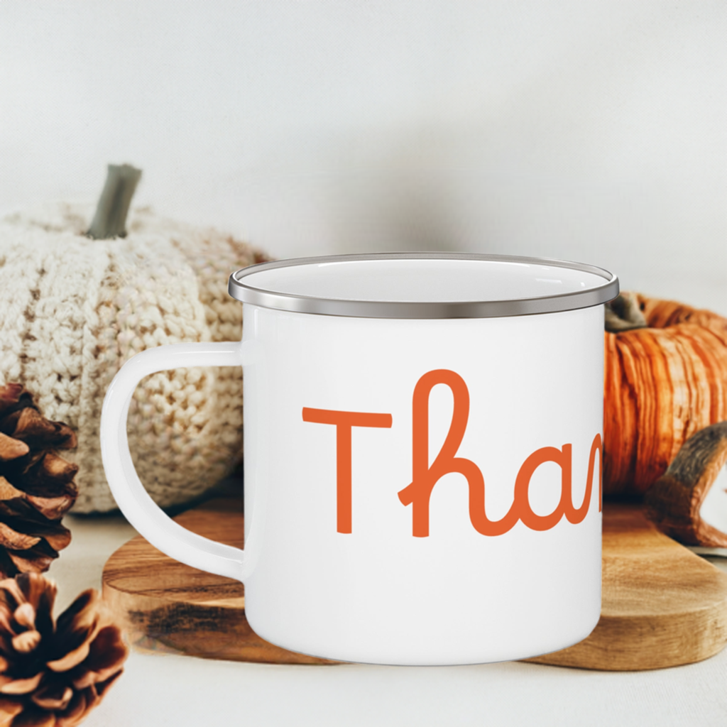 A white stainless steel camping mug with orange 'THANKFUL' text placed on a wooden stump with  pumpkins background.