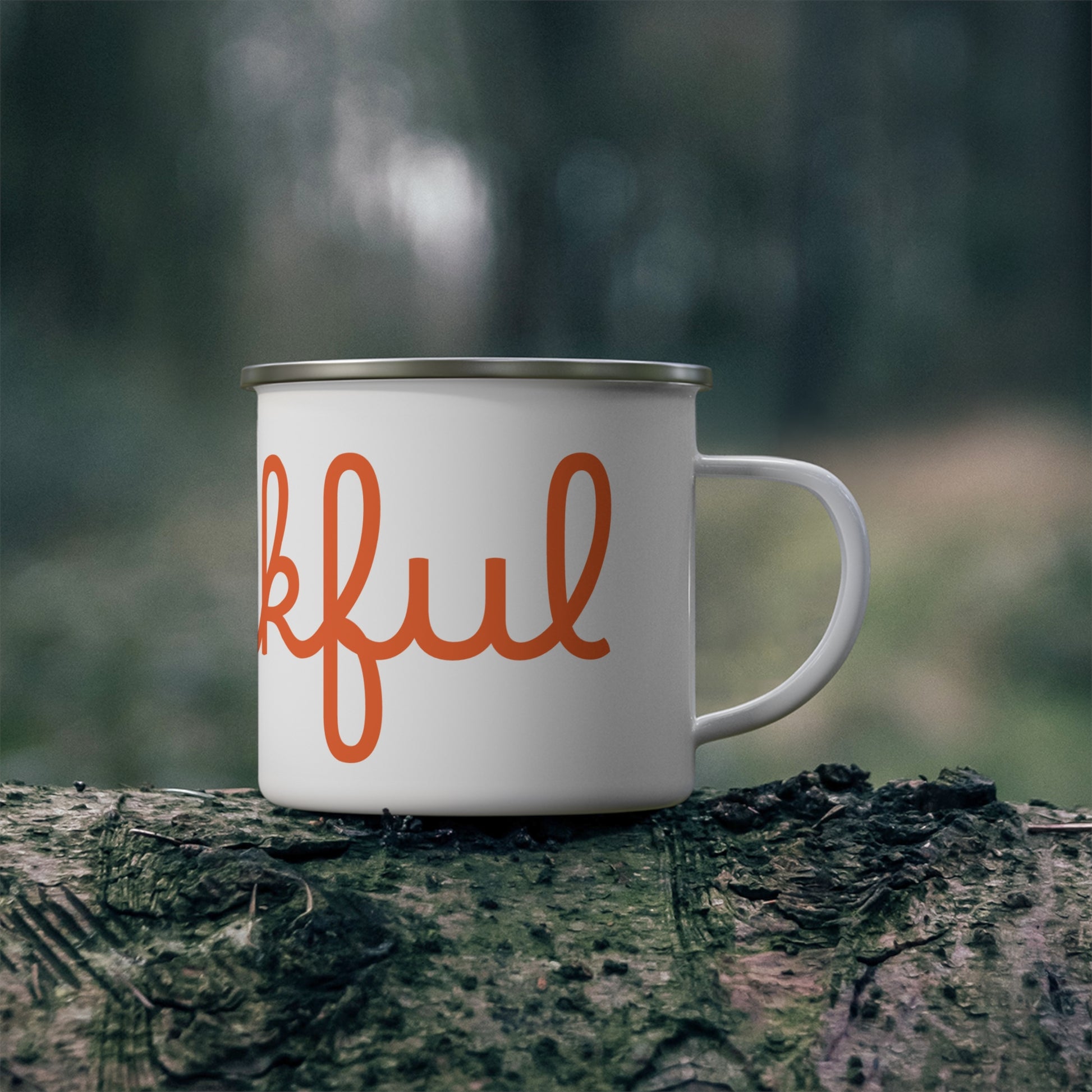 A white stainless steel camping mug with orange 'THANKFUL' text placed on a wooden stump with a hot steam background.