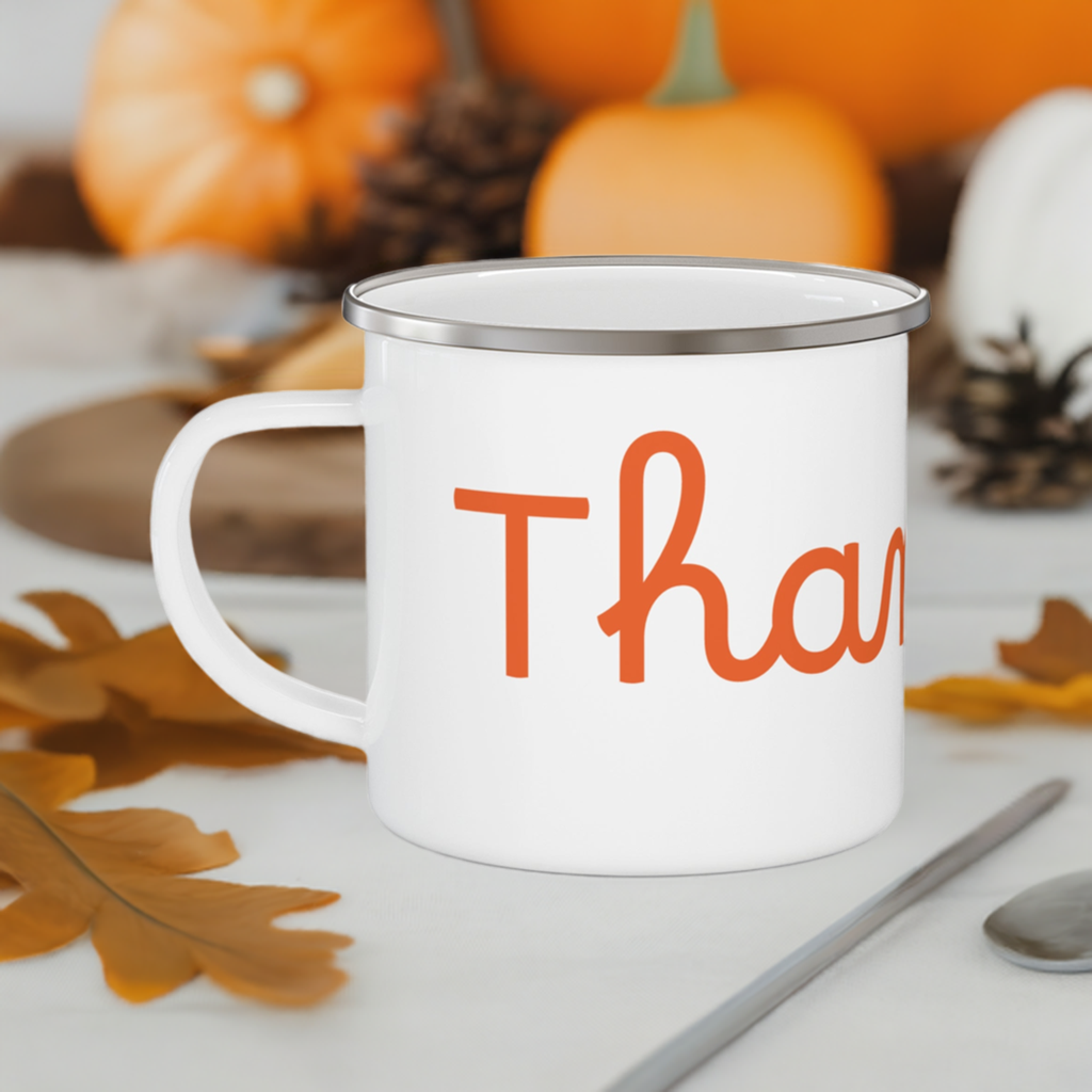 A white stainless steel camping mug with orange 'THANKFUL' text placed on a ceramic surface with leaves and pumpkins background.
