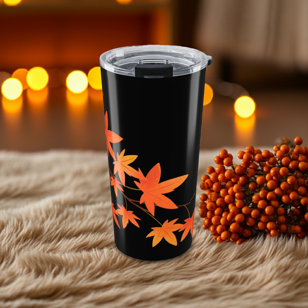 Black tumbler with orange leaf design on a textured surface with blurred lights in the background